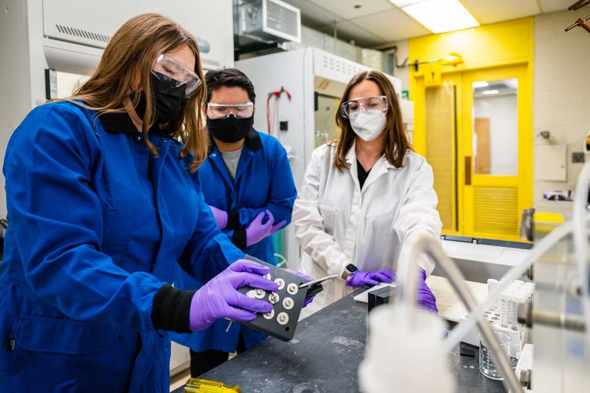 Three technicians in a lab with protective gear inspecting and instrument.